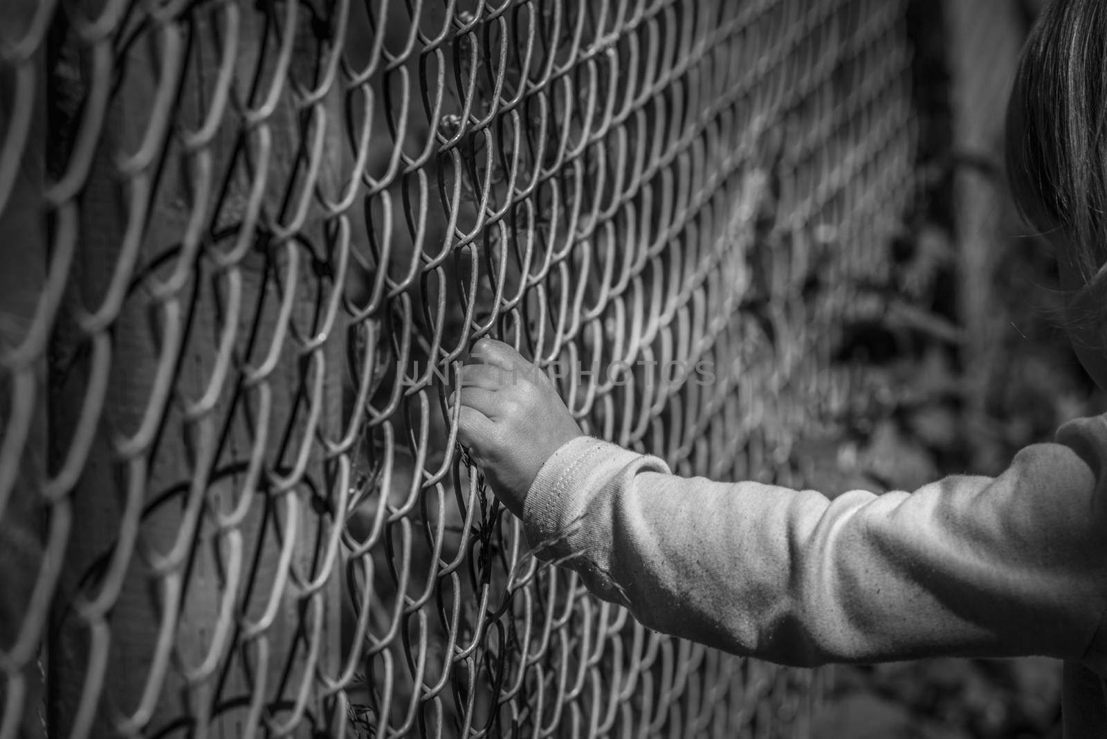 Black and white image of a little girl hand grabbing a metal fence, depicting drama
