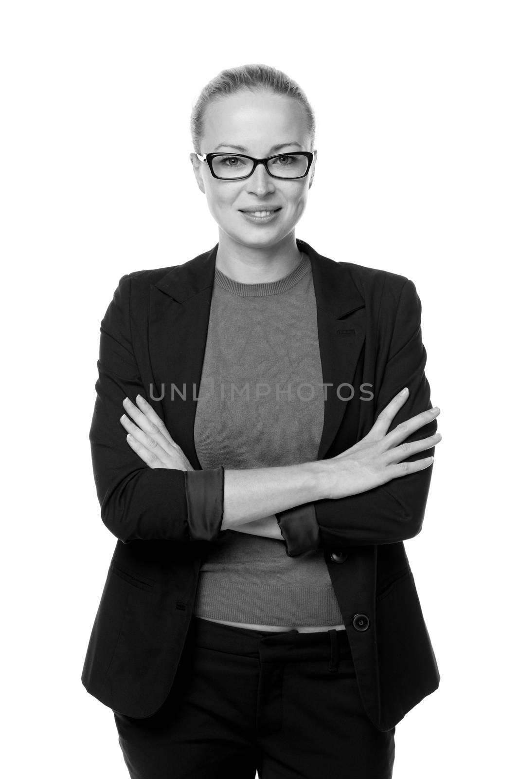 Black and white portrait of beautiful smart young businesswoman in business attire wearin black eyeglasses, standing with arms crossed against white background.