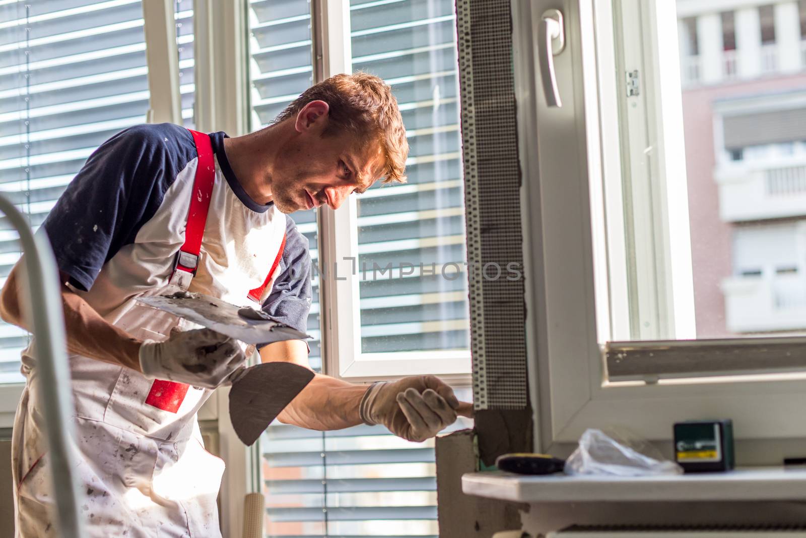 Construction worker wearing worker overall with wall plastering tools renovating apartment house. Plasterer renovating indoor walls and ceilings with float and plaster. Construction finishing works.