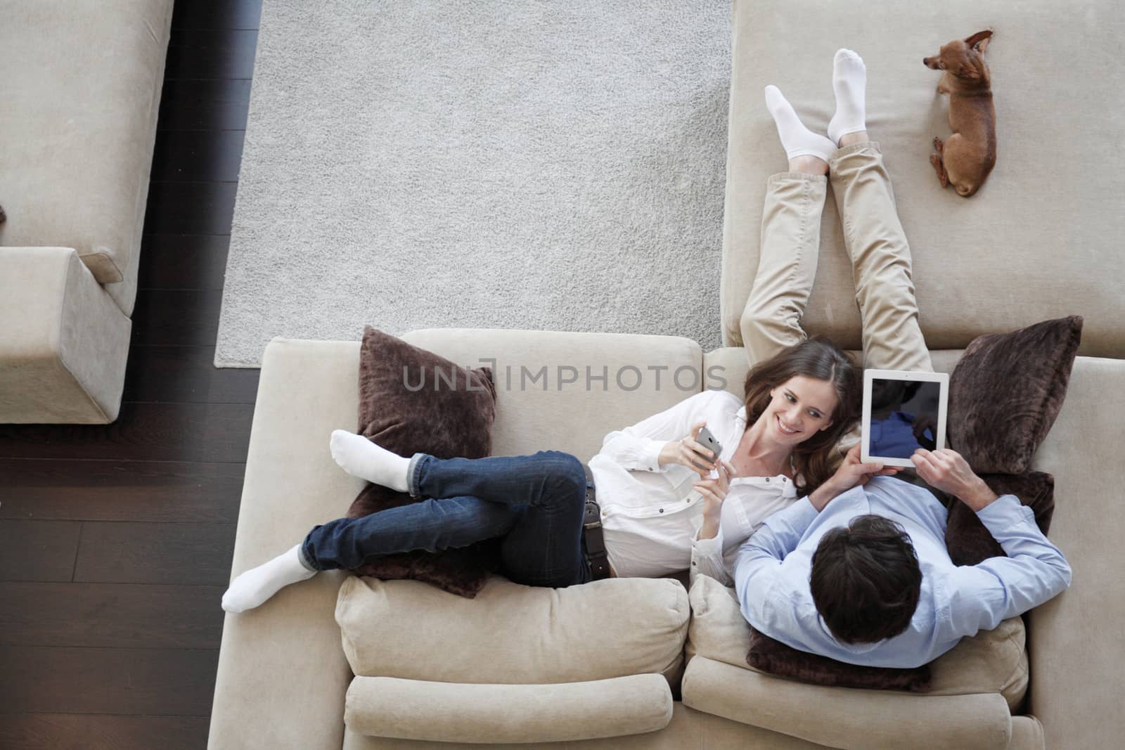 Couple using digital tablet at home sitting on sofa, top view