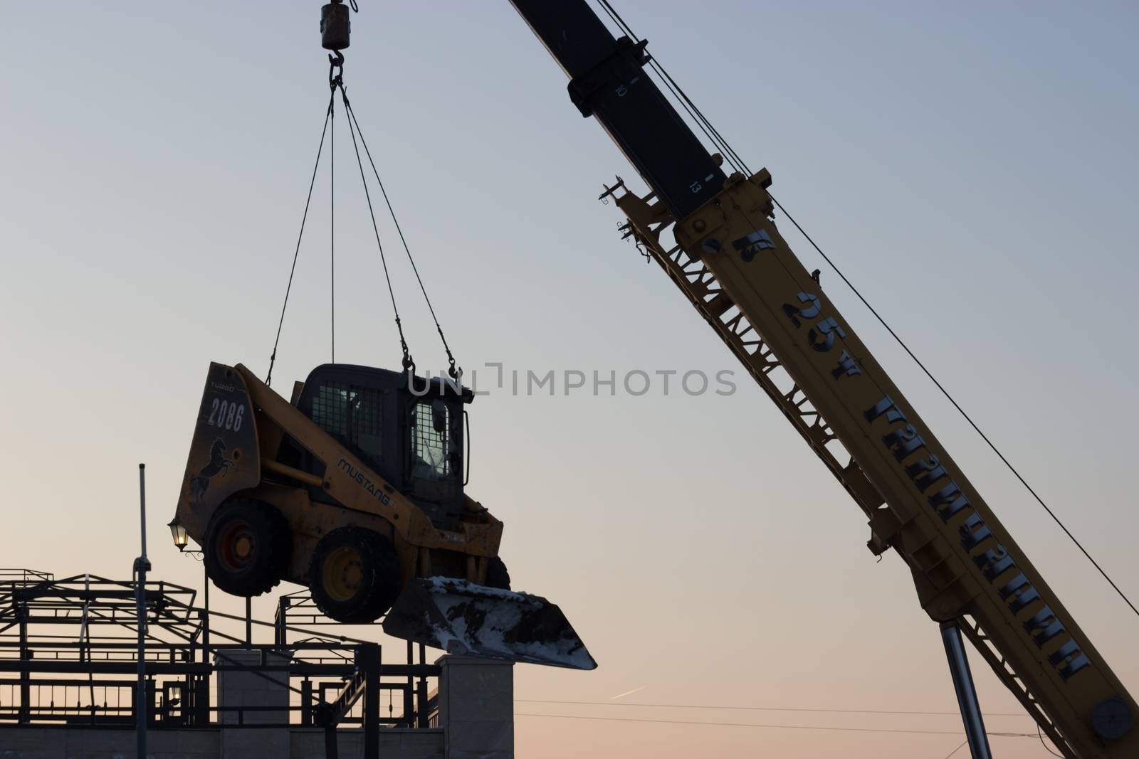 Industrial Crane operating and lifting an snow removal machine, twilight