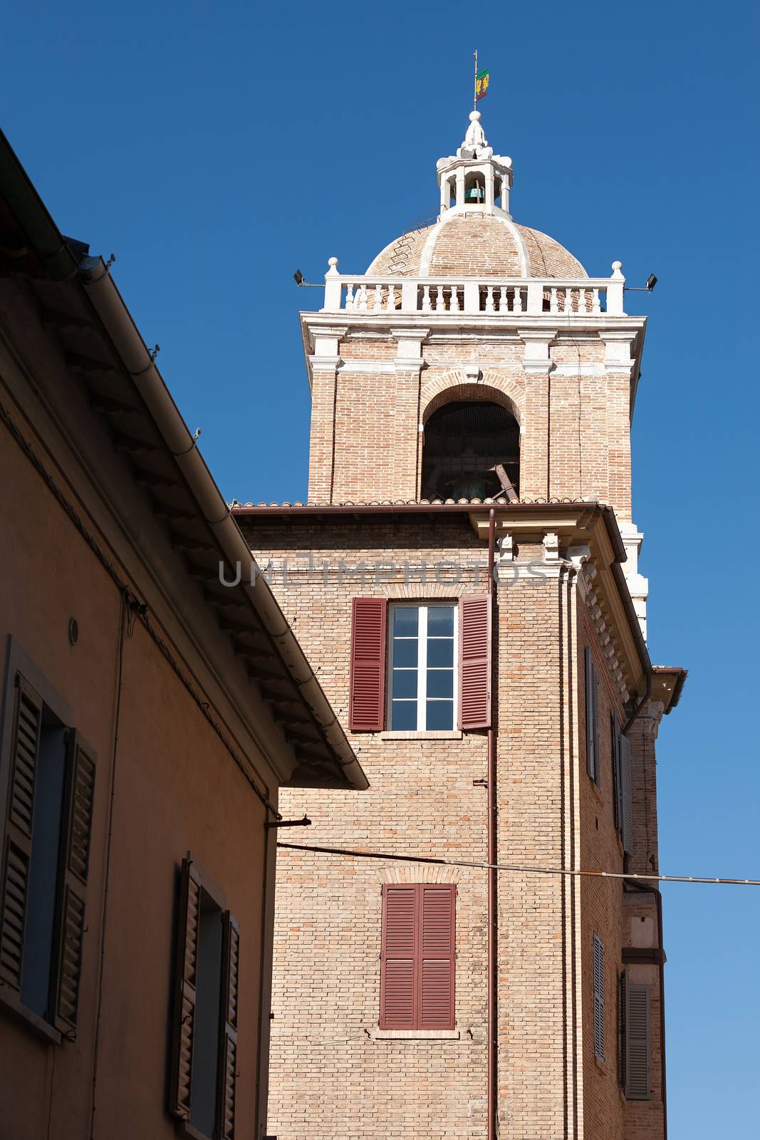 The bell tower of the town hall in Senigallia seen from a side under a blue sky.