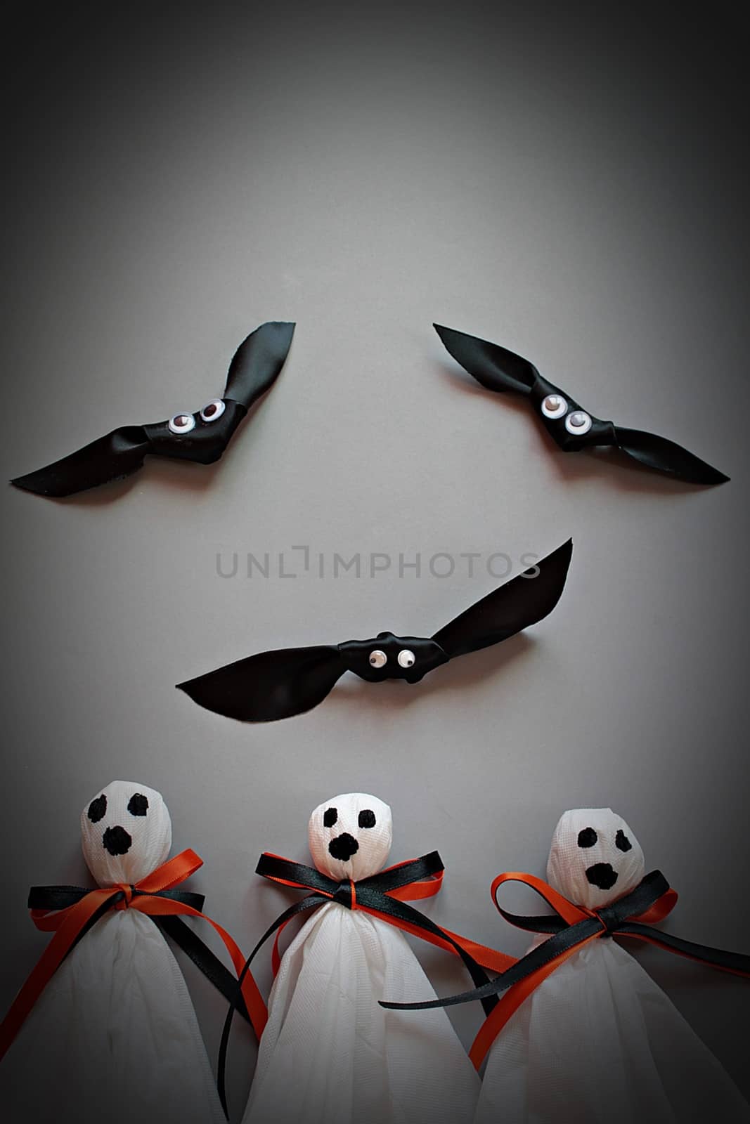 Halloween concept background : Three halloween ghosts DIY made from white tissue paper, black and orange ribbon and three bats DIY made form black ribbon on gray background