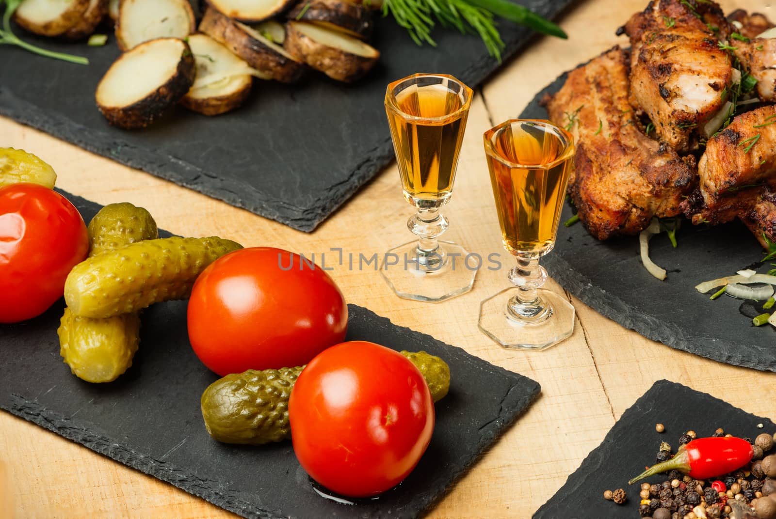 Fried meat, potatoes, vegetables on black slate plates and two shot glasses with cognac by fotooxotnik