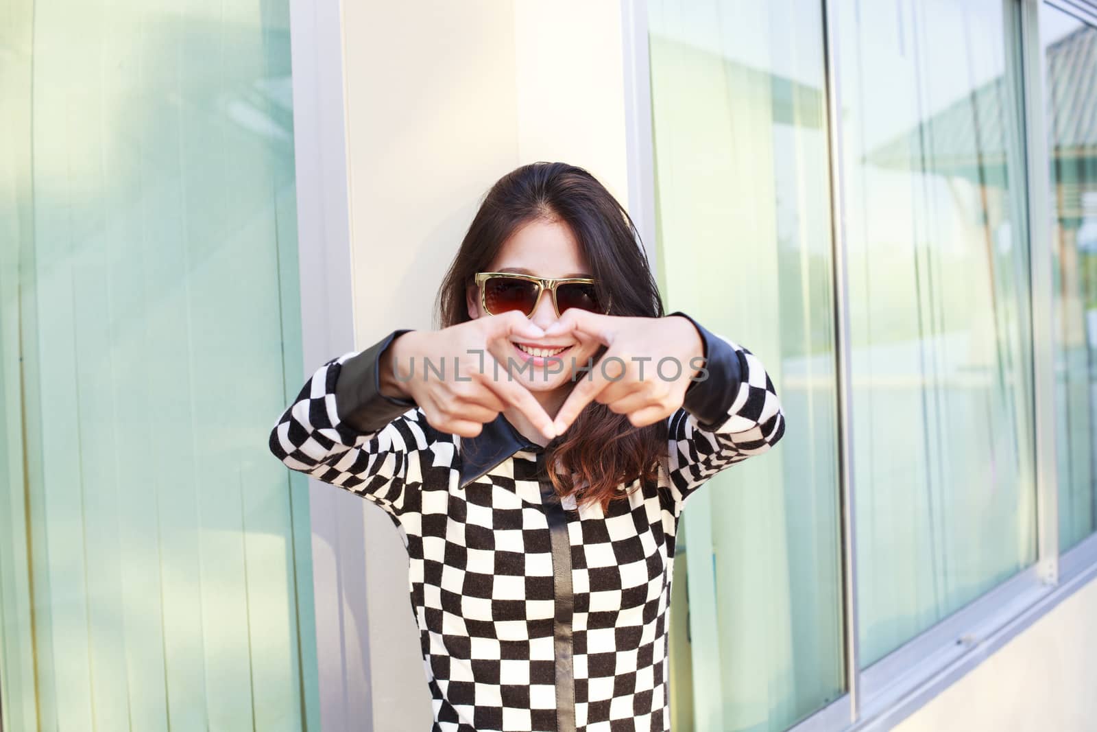 portrait of young beautiful hipster woman wearing sun glasses making heart symbol by finger hand