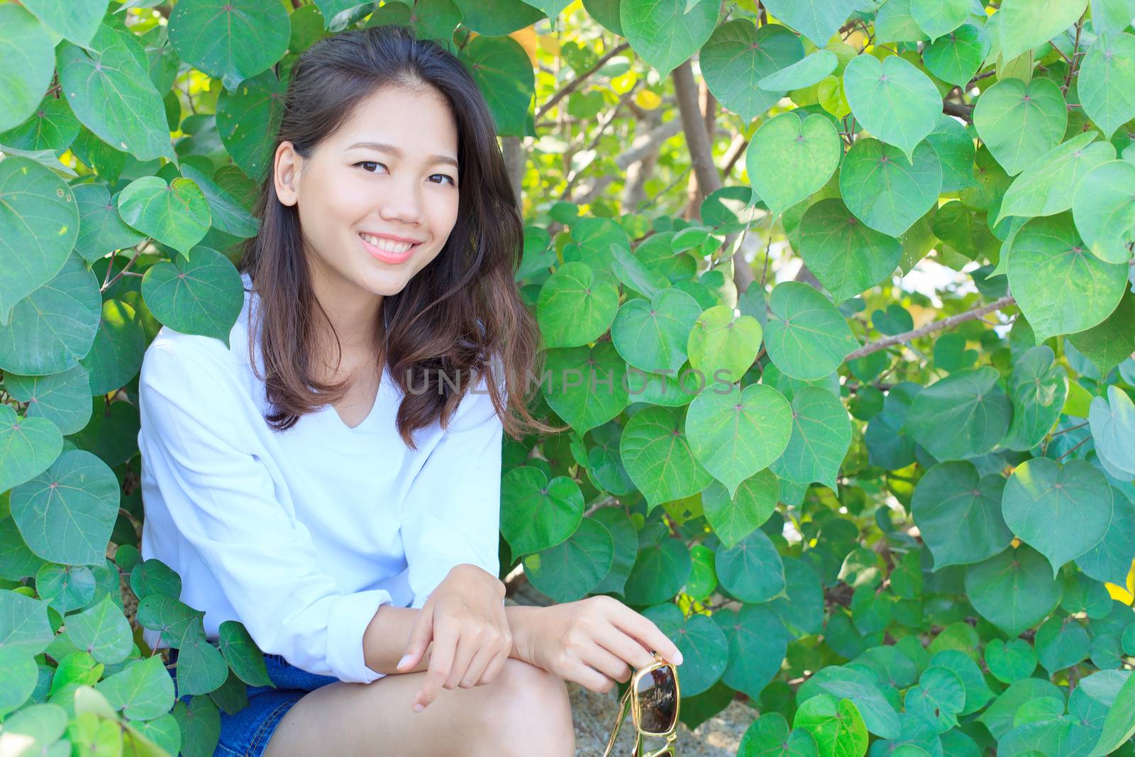 portrait of pretty woman sitting in green leaves bush and smilin by khunaspix