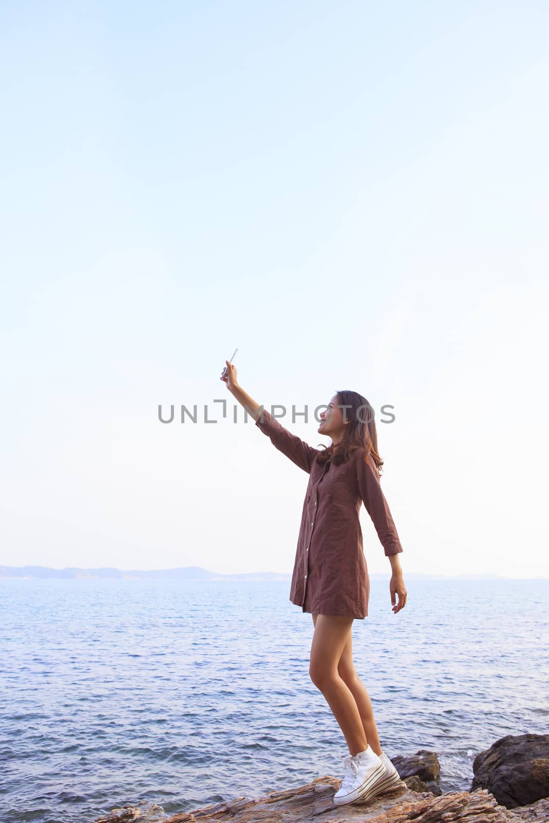 portrait of young beutiful woman rising up smart phone to sky us by khunaspix