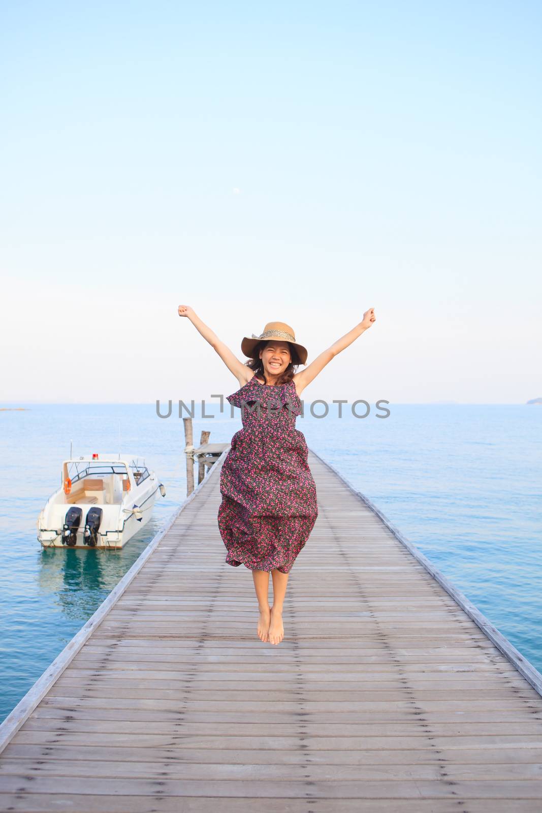 portrait of beautiful woman wearing long dress and wide straw hat jumping on wood pier use for people relaxing activities on sea beach and holiday vacation on destination