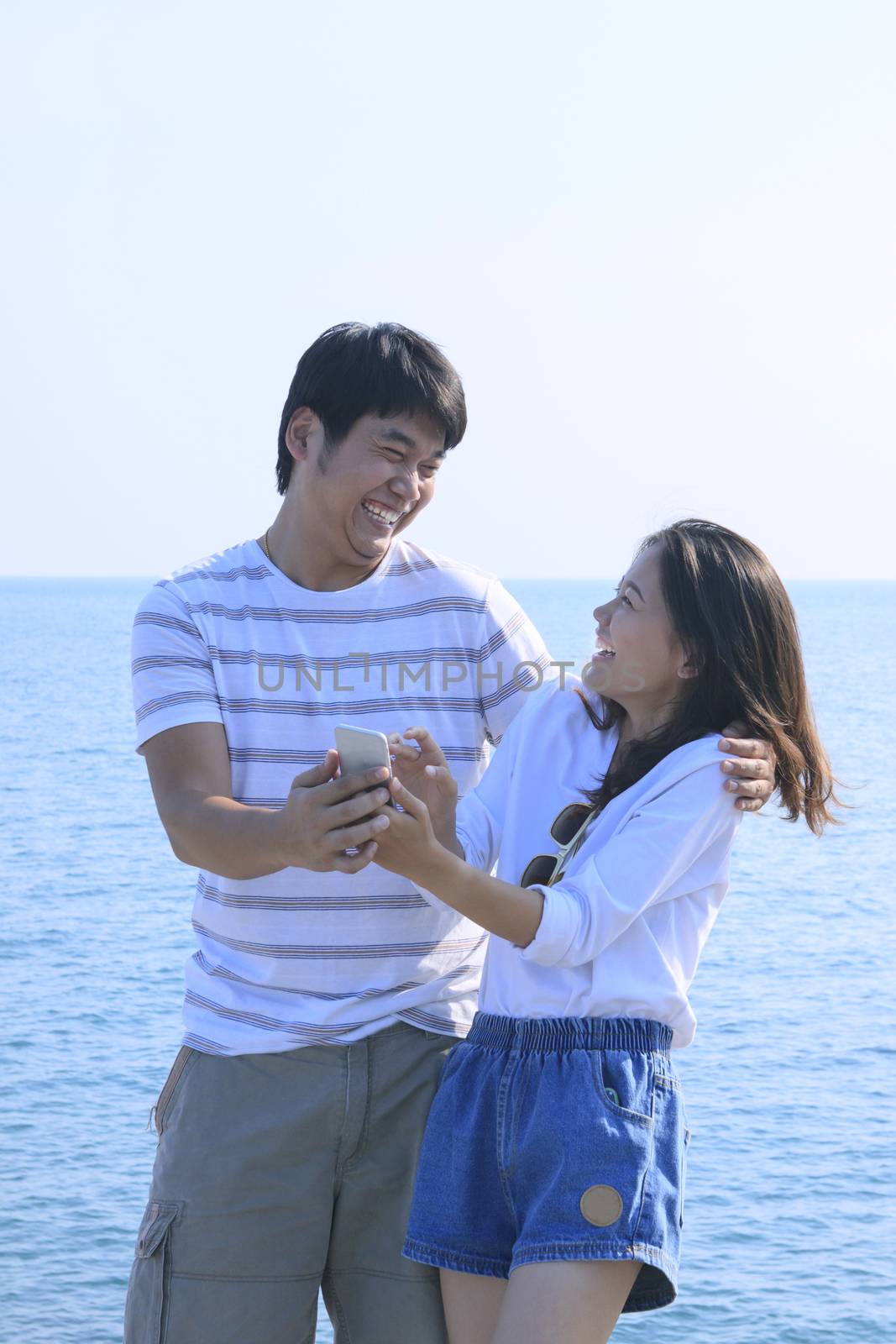 young man and woman with mobile phone in hand  standing at sea side and laughing happy emotion