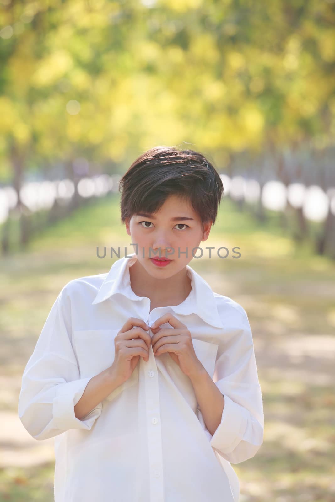 portrait of beautiful young asian woman wearing white shirts standing in blooming yellow flowers park and looking to camera with eyes contact 