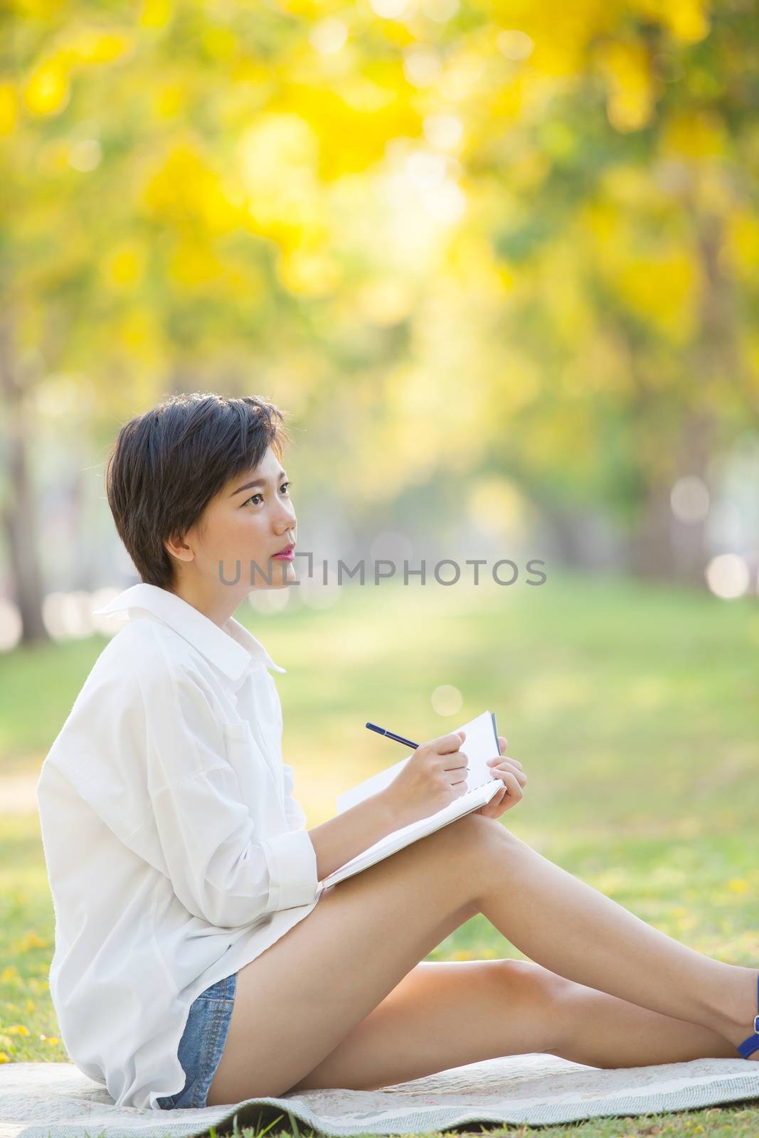 young woman sitting on green grass park with pencil and note book in hand thinking something ,project,dream,hope,solution in future