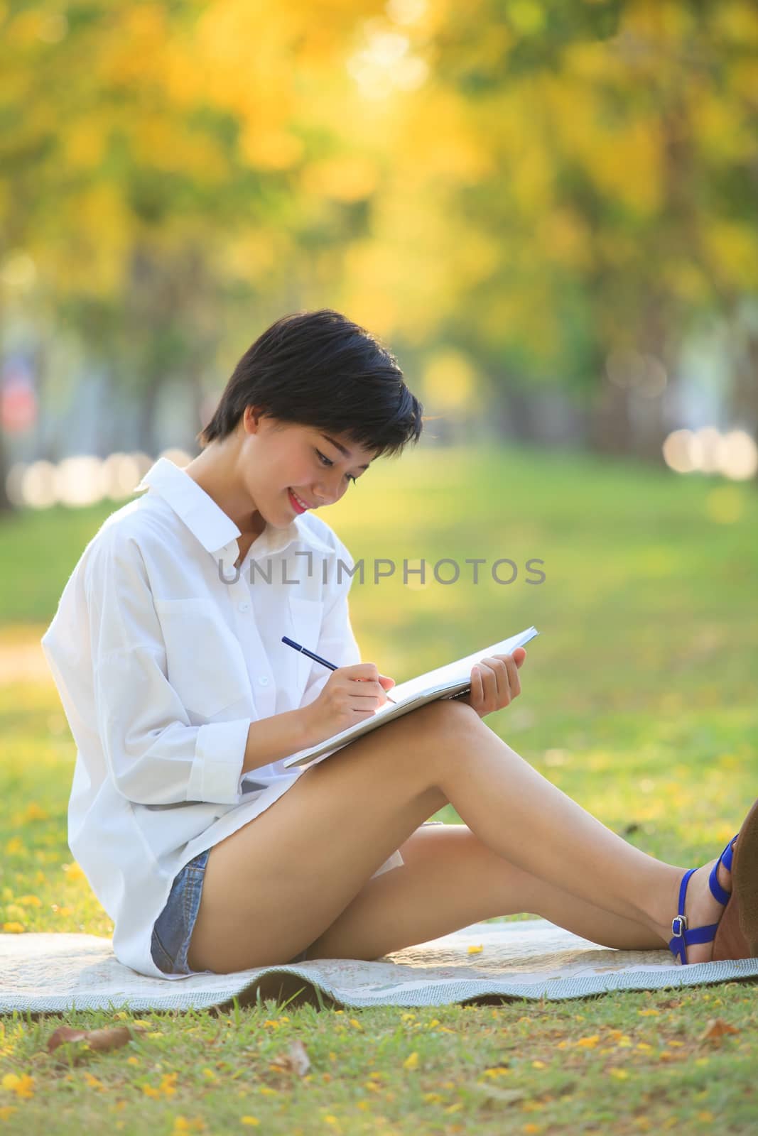 young beautiful asian woman writing text in diary book in yellow flowers park use for people education and relaxing in summer holiday and young activities