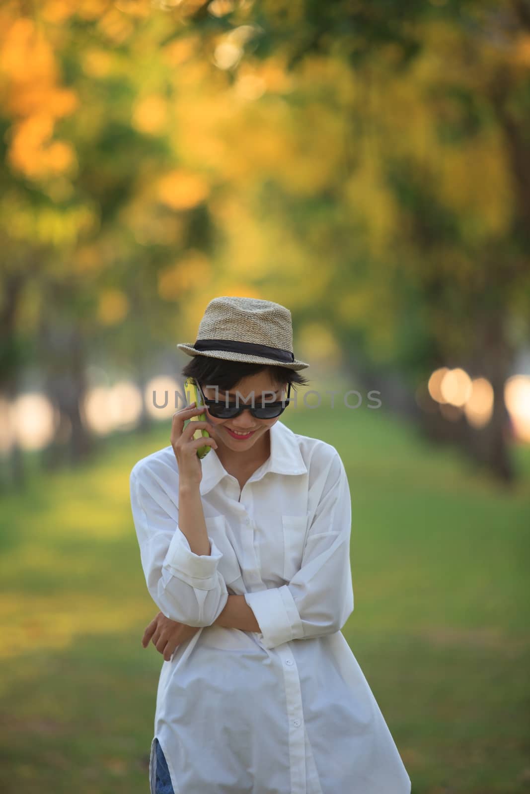 beautiful young woman wearing sun glassea nd straw hat talking on mobile phone with happiness emotion against blurry yellow flower in park use for people and modern life in digital connecting technology