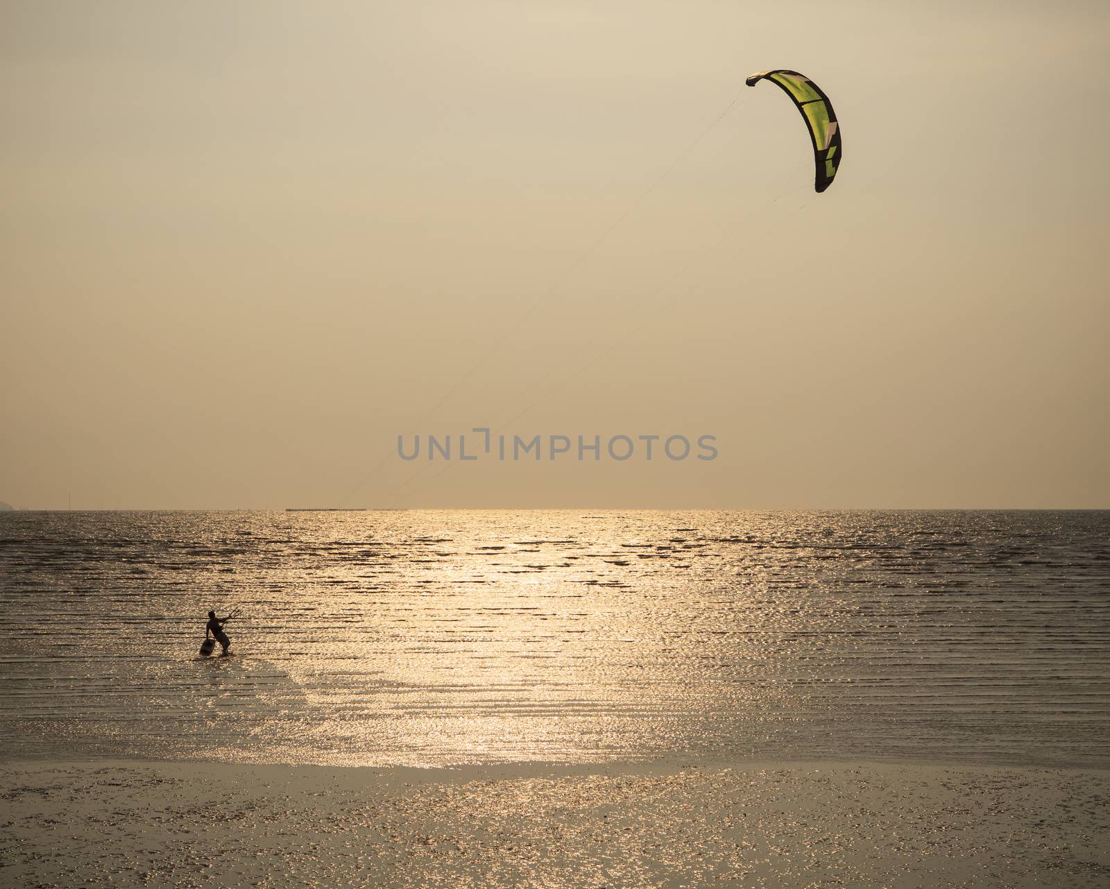 man with kite surving standing in sea water against evening sun  by khunaspix
