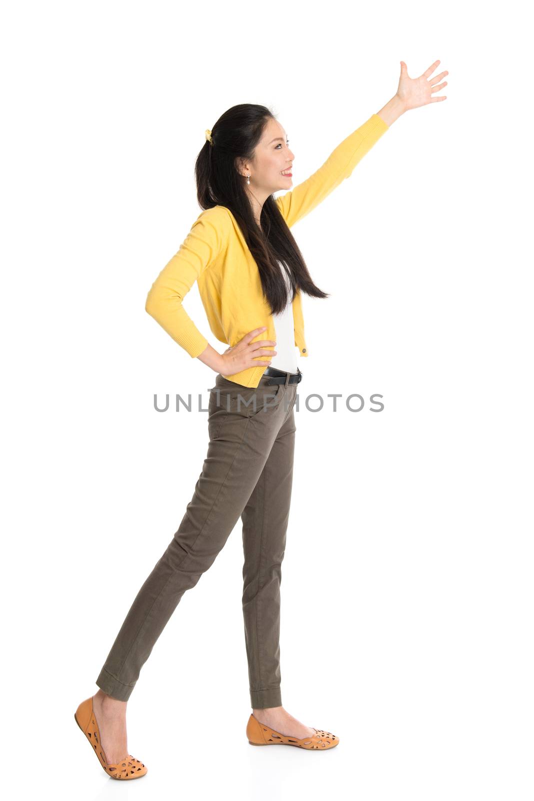 Full length Asian woman hand raised reaching or grabbing something, standing isolated on white background.