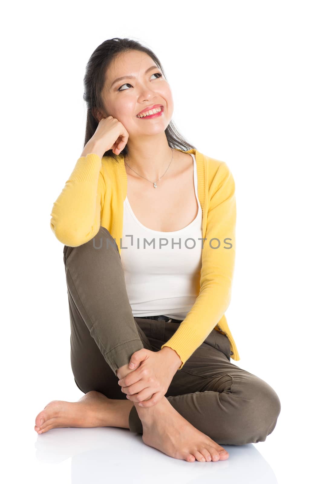 Full length pensive Asian girl sitting on floor smiling and thinking, looking upward, isolated on white background.