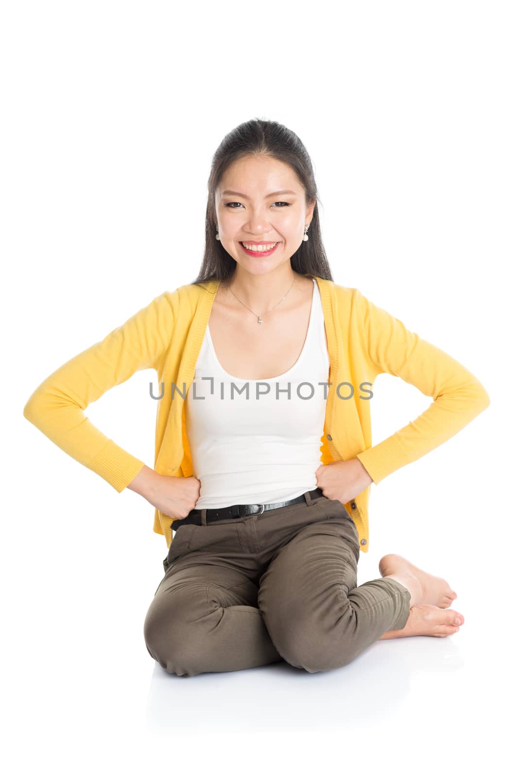 Full length casual Asian female sitting on floor smiling and looking at camera, isolated on white background.