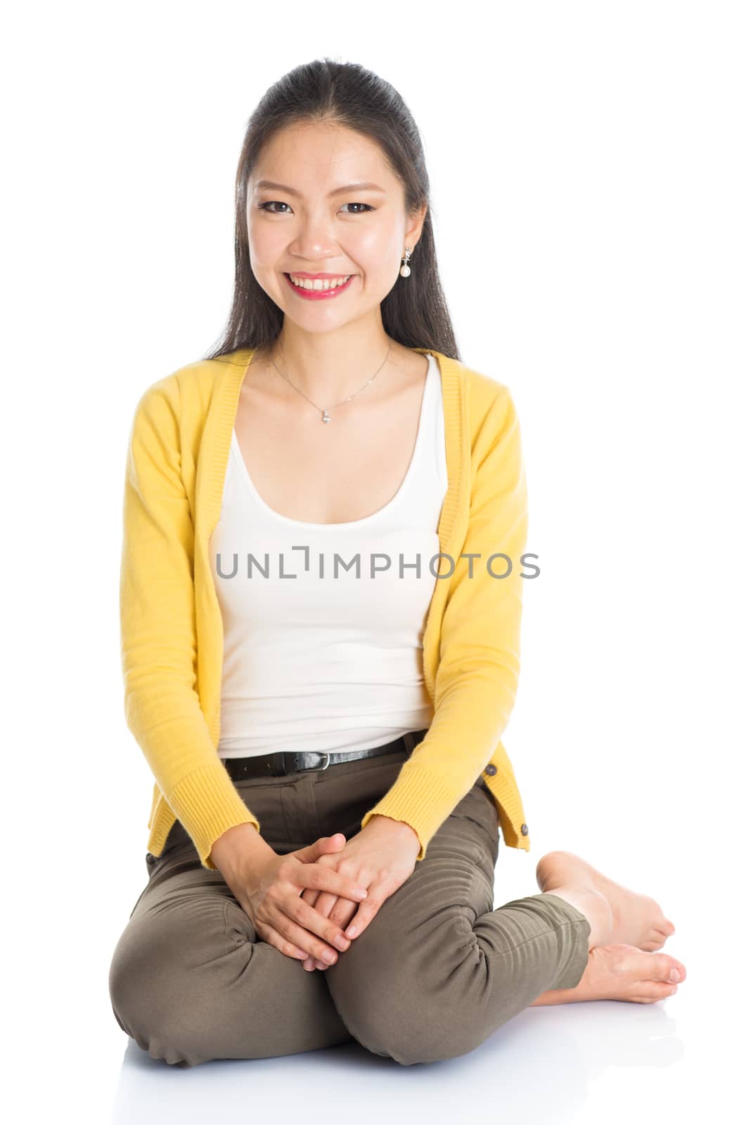 Full length casual Asian girl sitting on floor smiling and looking at camera, isolated on white background.