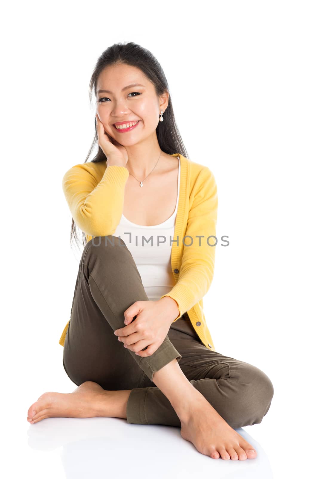 Full length Asian female sitting on floor smiling and looking at camera, isolated on white background.