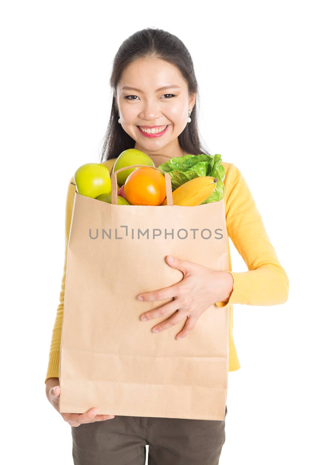 Happy young Asian woman shopper, hands holding shopping bags filled with groceries and smiling, isolated standing on white background.