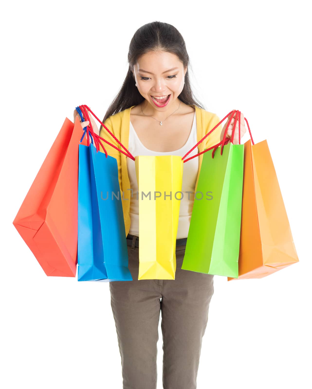 Happy young Asian female shopper, hands holding shopping bags and smiling, isolated standing on white background.