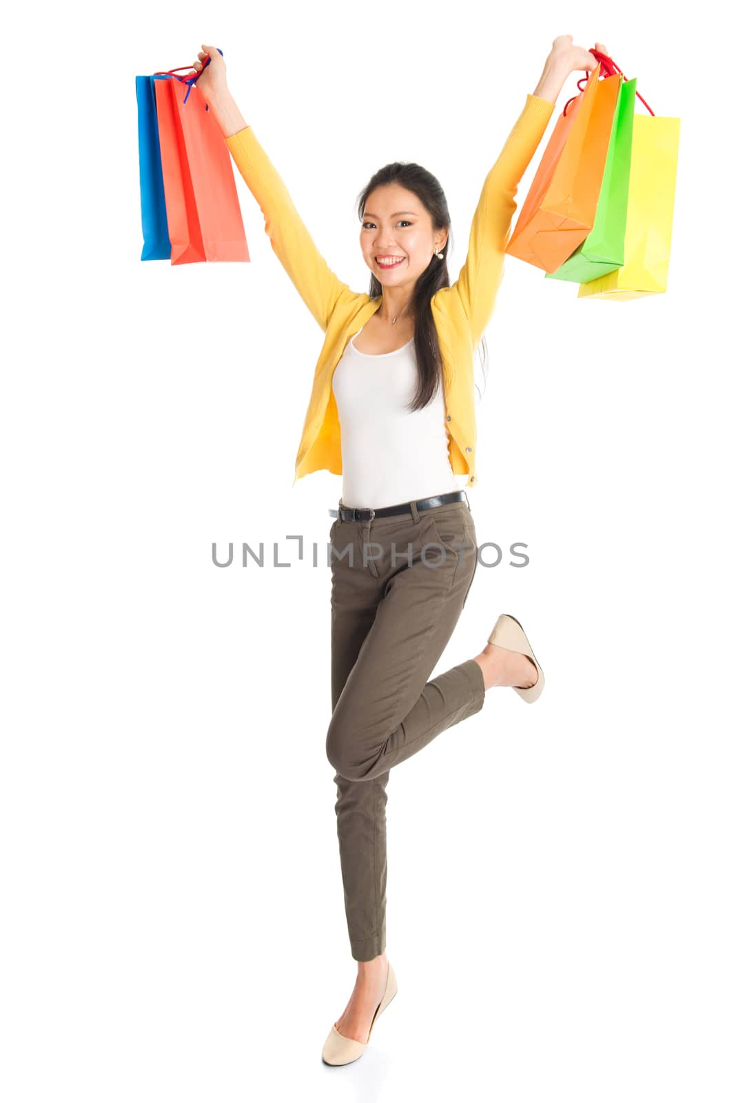 Happy young Asian girl shopper, hands outstretched holding shopping bags and smiling, full length isolated standing on white background.