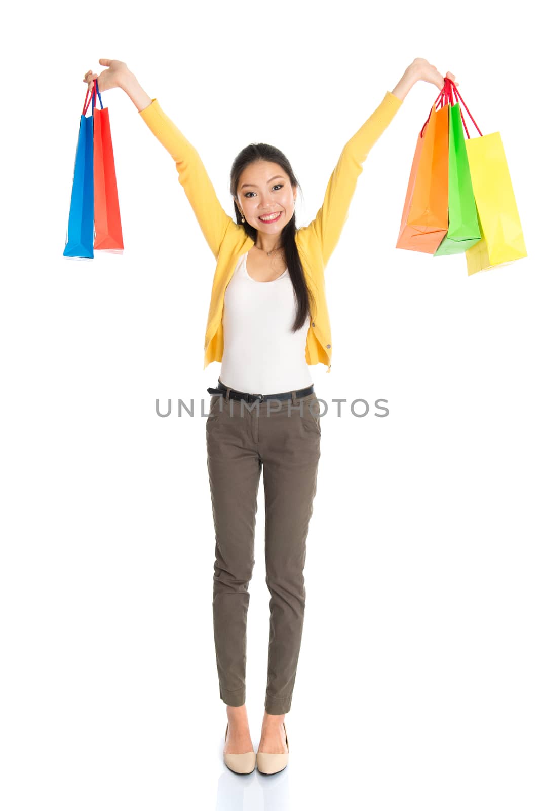 Happy young Asian woman shopper, hands outstretched holding shopping bags and smiling, full length isolated standing on white background.