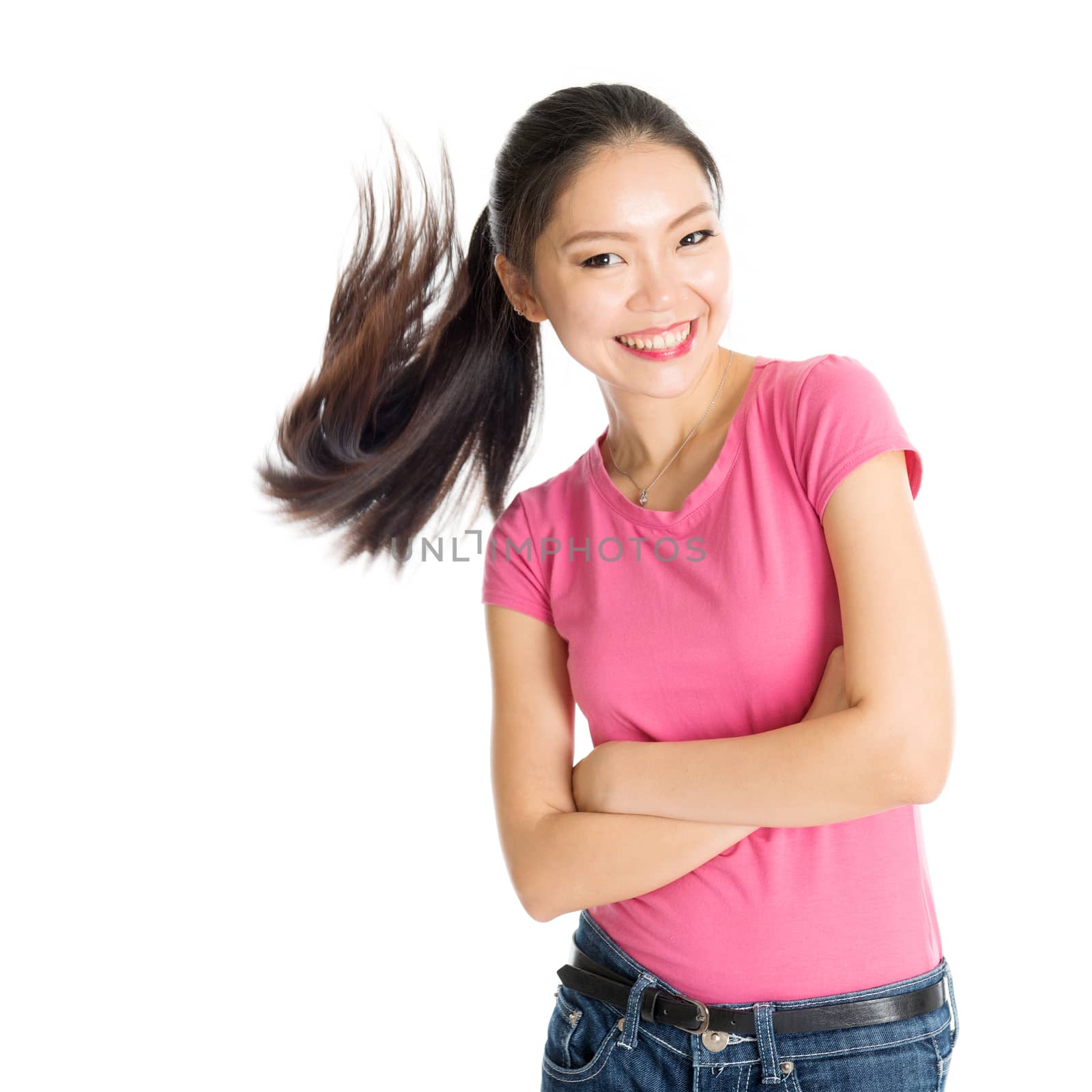 Portrait of happy young Asian woman in pink shirt and jeans with flying ponytail hair, standing isolated on white background.