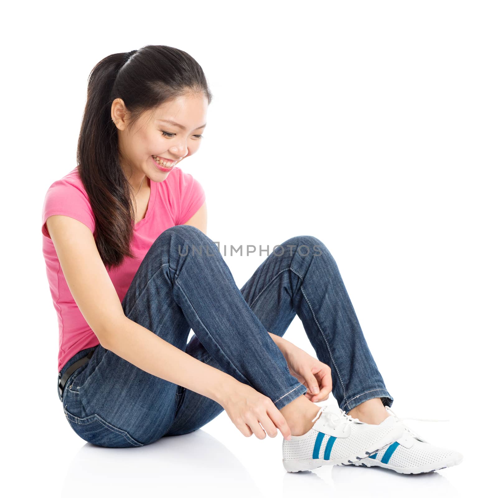 Portrait of young Asian girl in pink shirt and jeans wearing shoe, full body seated isolated on white background.