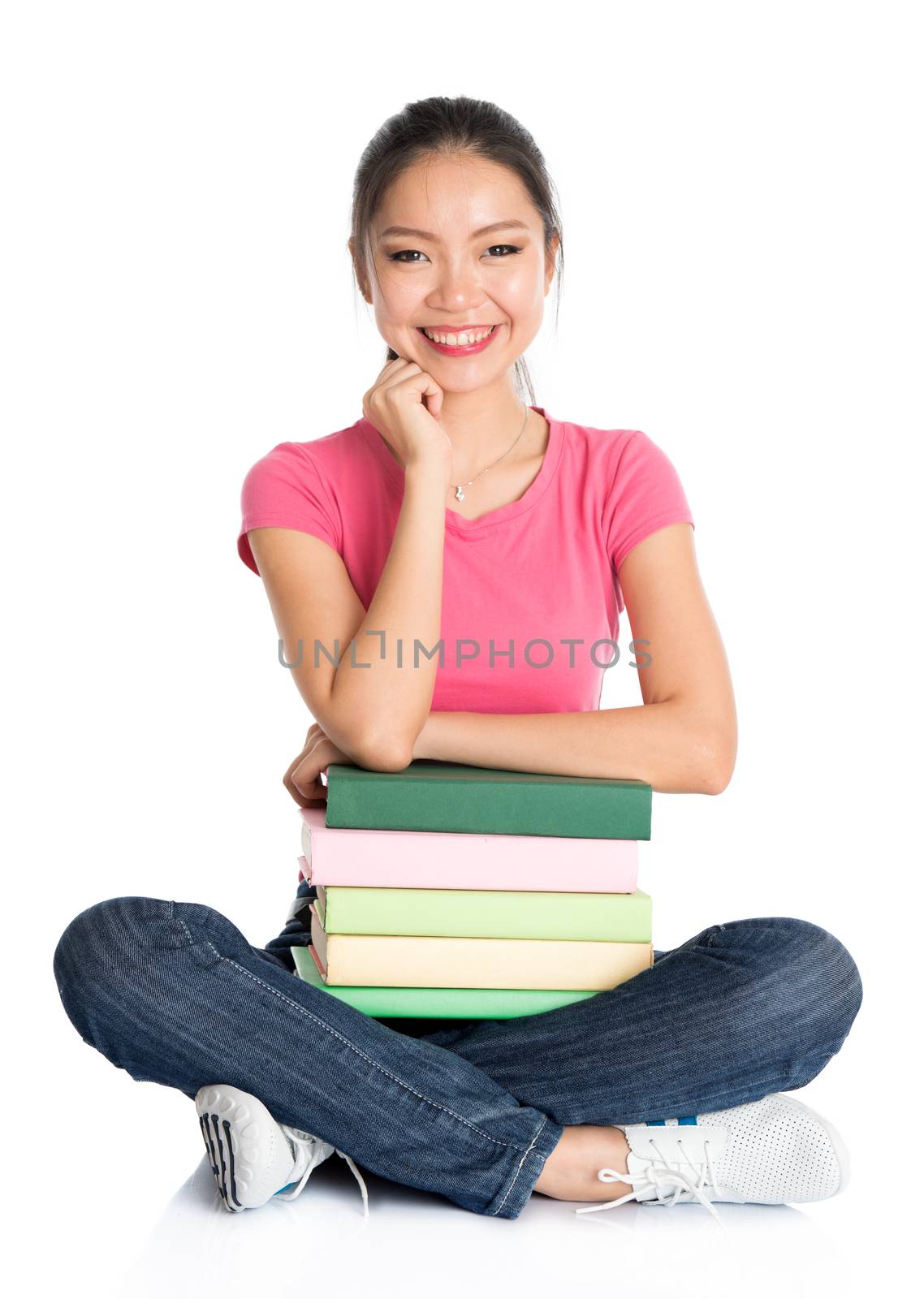 Full body young Asian college girl student in pink shirt with stack of textbooks, seated on floor, full length isolated on white background.