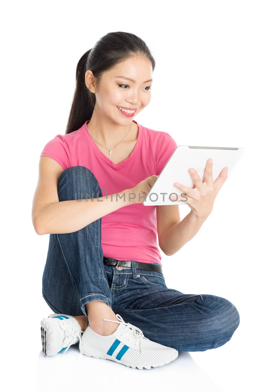 Full body young Asian girl in pink shirt using digital tablet pc, seated on floor, full length isolated on white background.