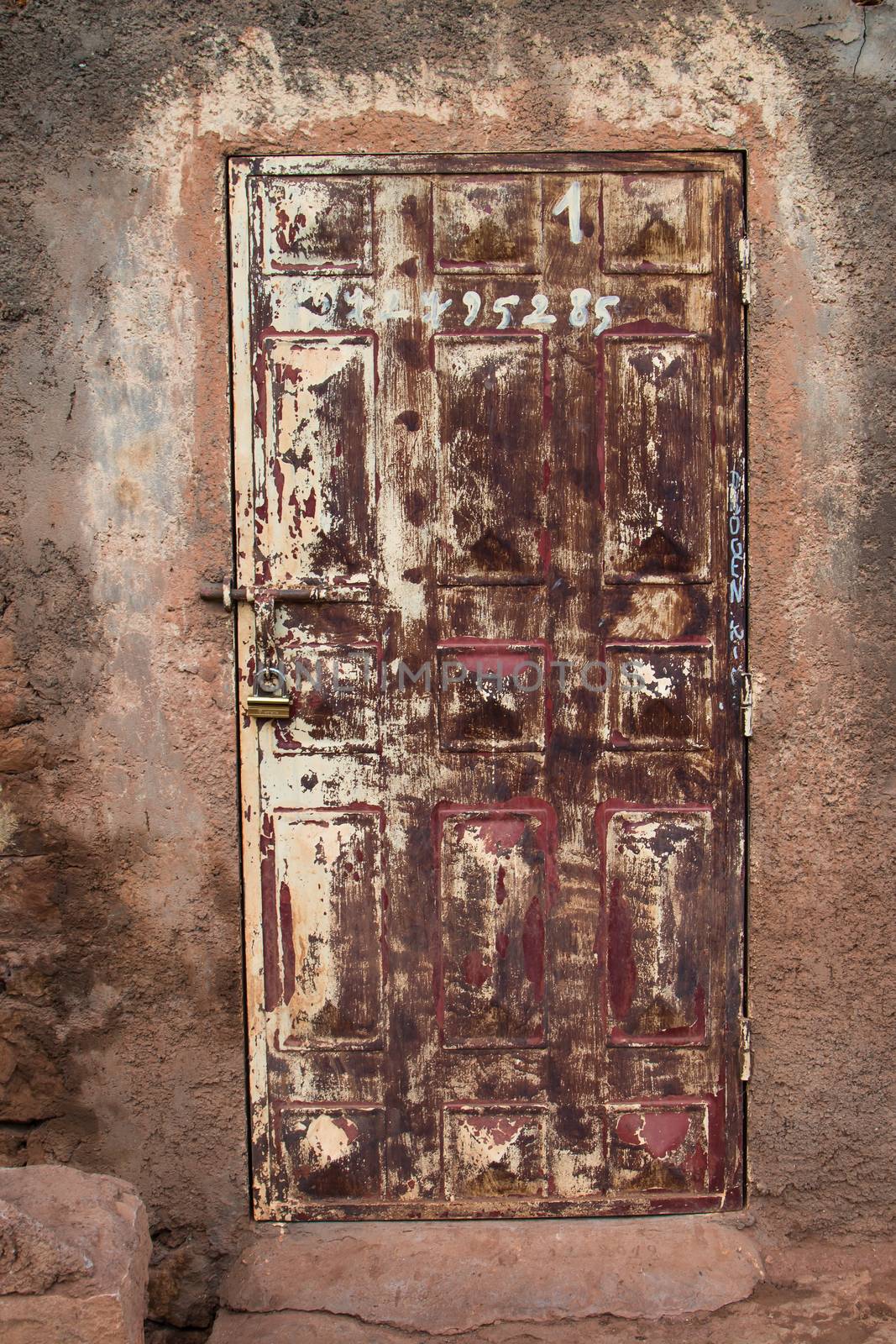 Wooden door with a very worn painting, the same as the wall around. Various numbers written on the door. Photo taken in Morocco.