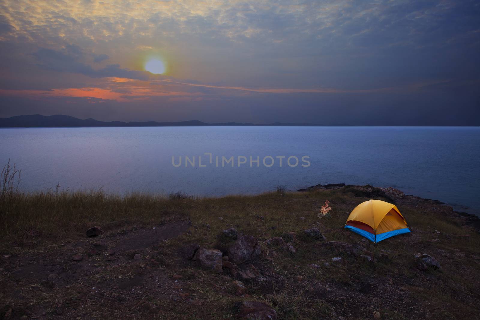 camping tent on rock mountain with sun rising on dramatic sky by khunaspix