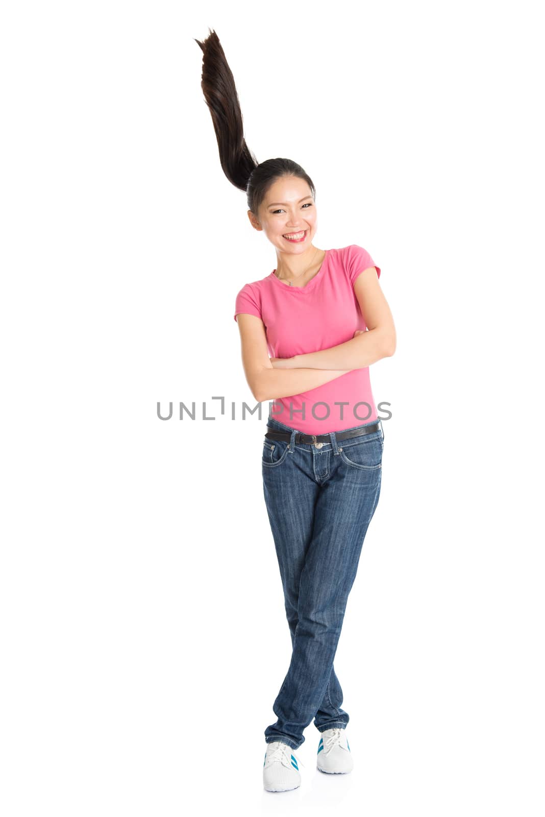Portrait of young Asian woman in pink shirt and jeans with flying ponytail hair, full length standing isolated on white background.