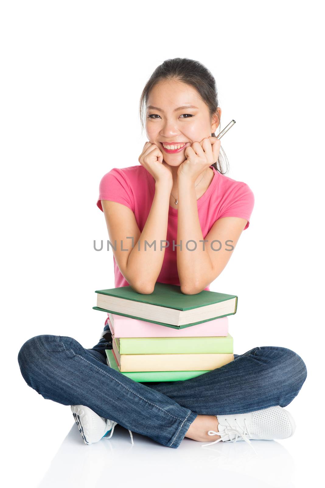 Full body young Asian girl in pink shirt with textbooks, seated on floor, full length isolated on white background.