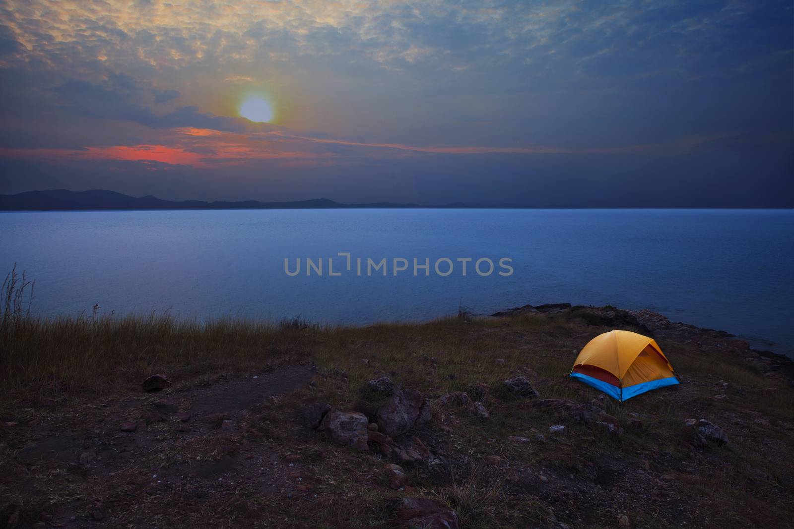 caping tent on mountain with sea coast infront and sun set on dramatic sky