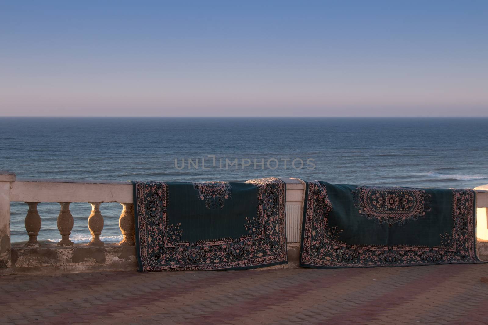 Like after a magic carpet ride, carpets getting dry hanging on the fence. Atlantic ocean in the background. City Sidi Ifni, Morocco.