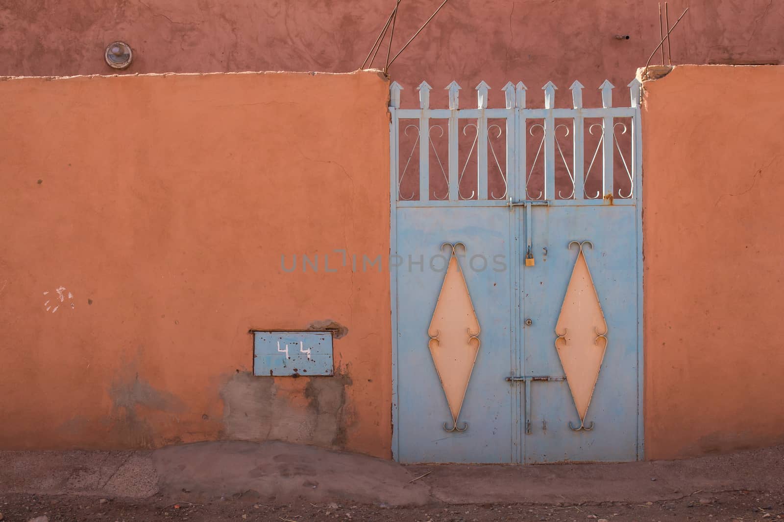 Orange fence with an enlightened blue iron gate. Photo taken in Morocco.