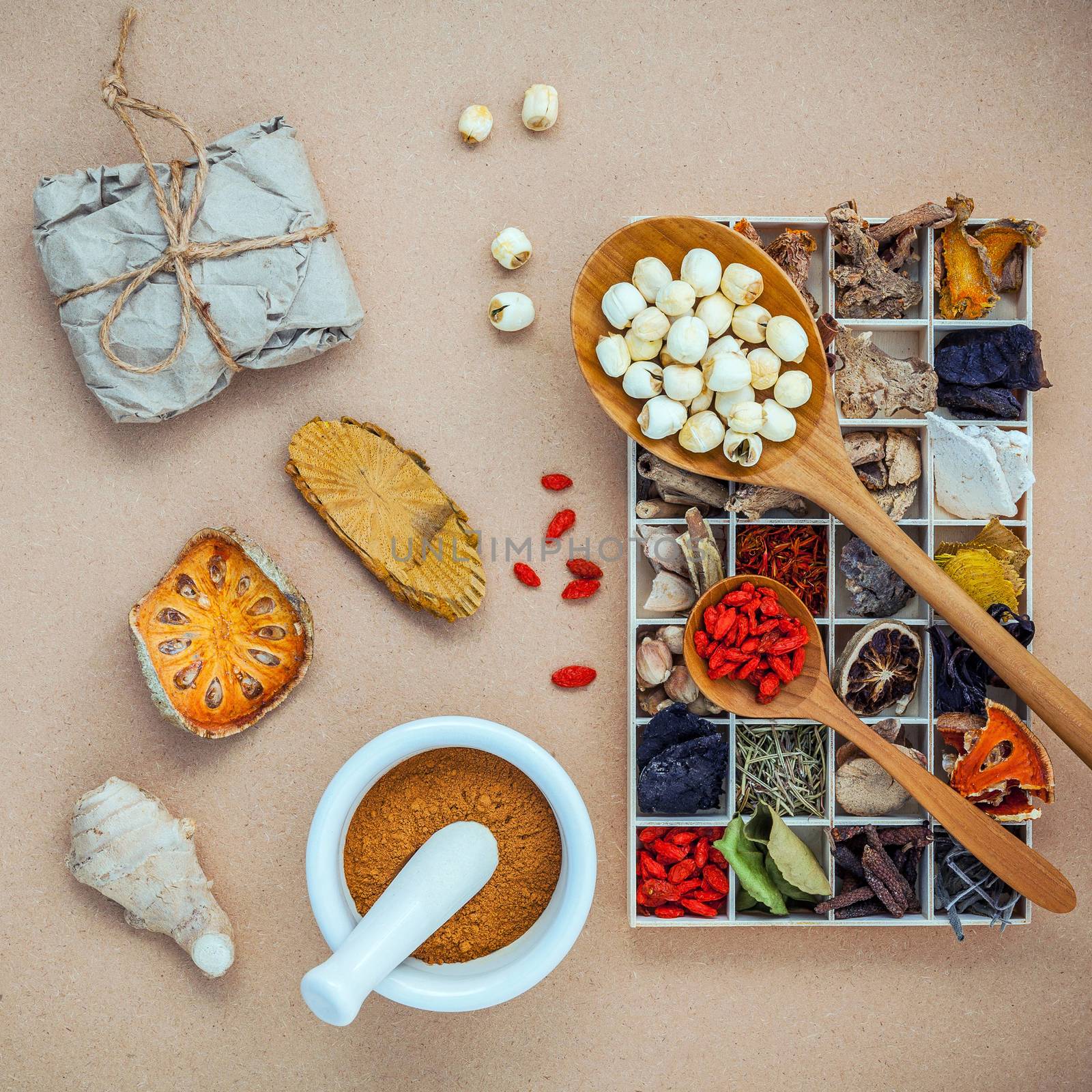 Alternative health care and herbal medicine. Dried various Chinese herbs in wooden box and lotus seeds in wooden spoon with white mortar on brown background flat lay.