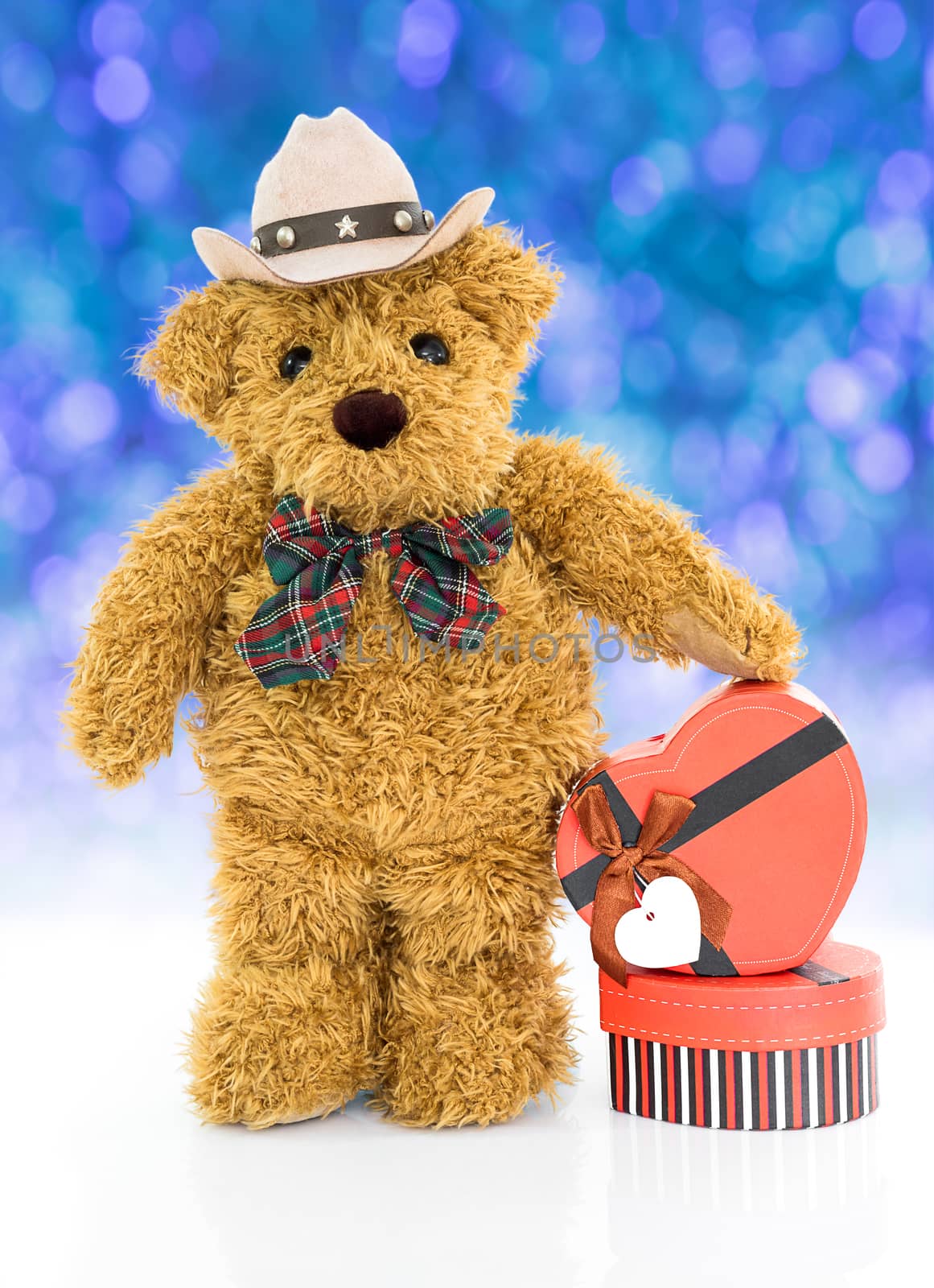 Teddy bear with 
Red heart shaped gift box on blue bokeh background