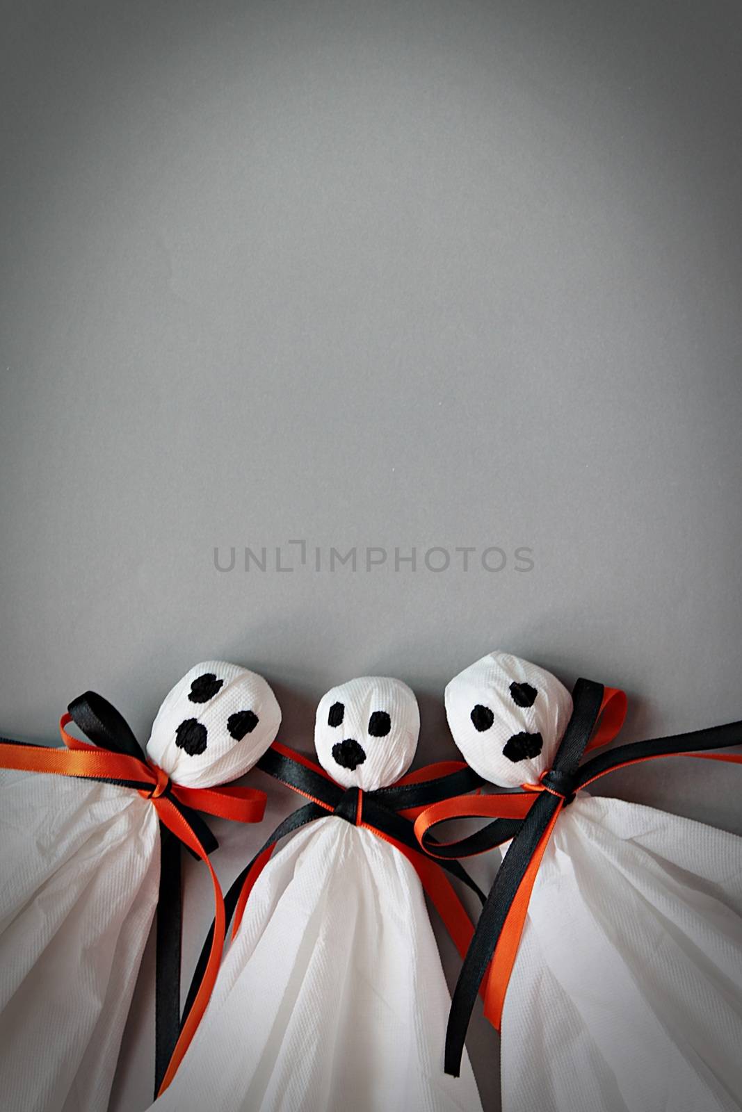 Halloween concept background : Three halloween ghosts DIY made from white tissue paper, black and orange ribbon on gray background