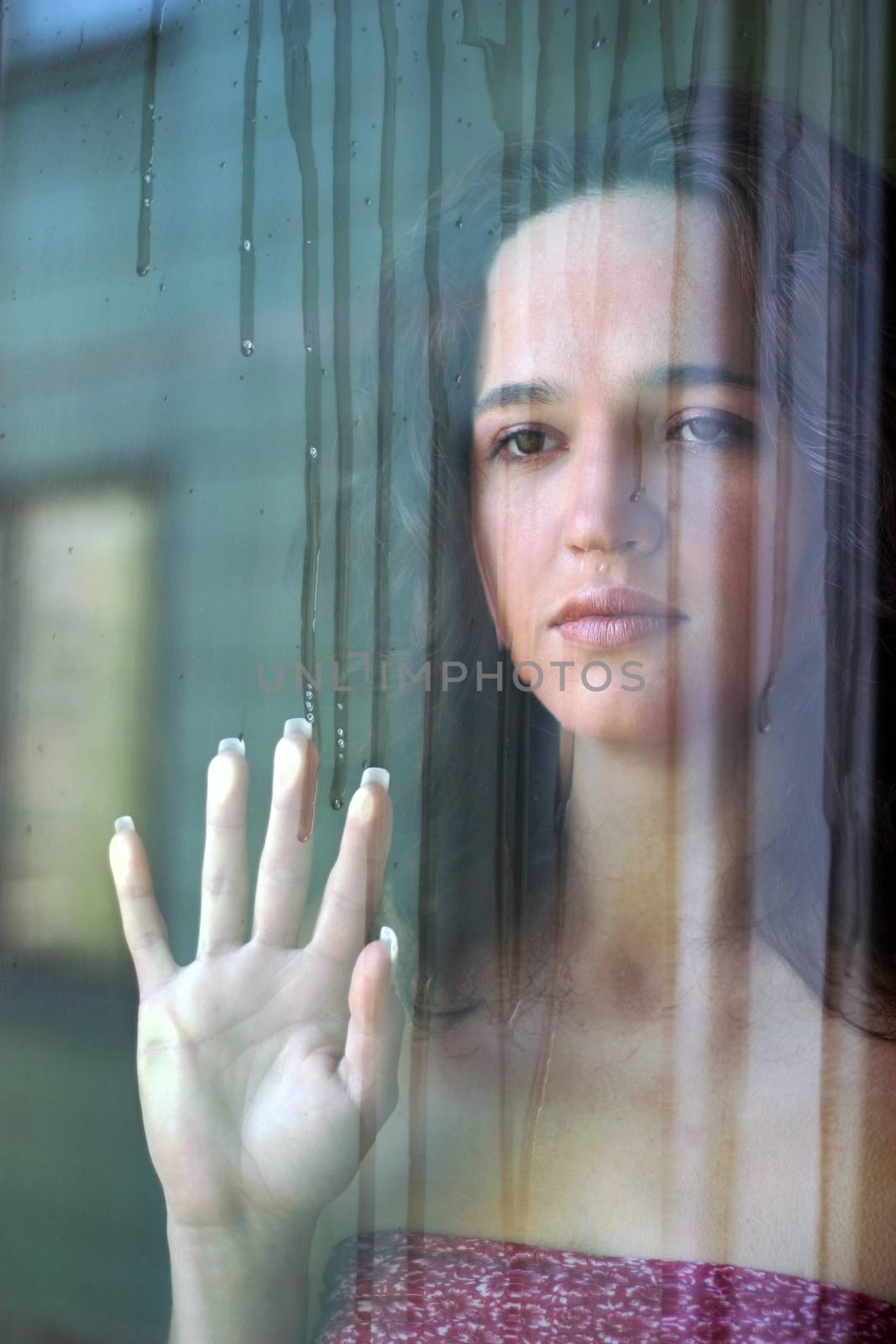 Woman with sad smile behind a wet window