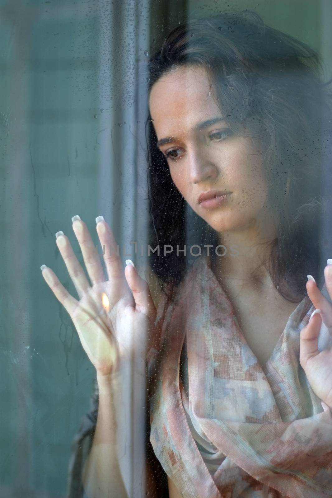 Woman with sad smile behind a wet window