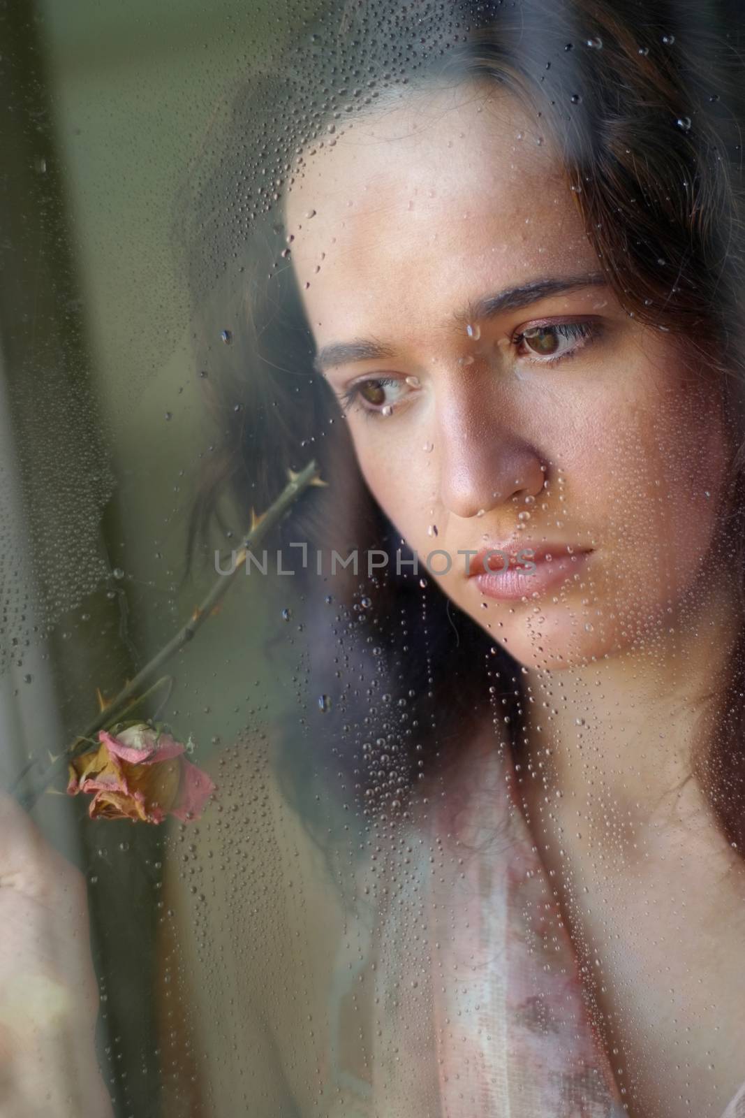 Woman with sad smile behind a wet window