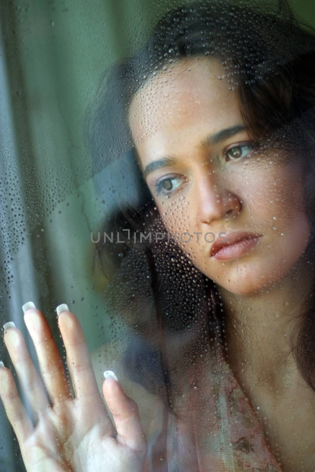 Woman with sad smile behind a wet window