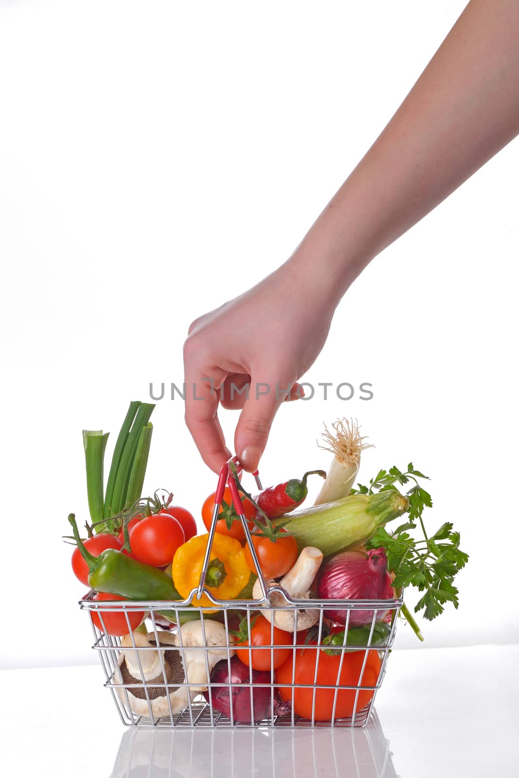 Hand with wire shopping basket full of fresh vegetables