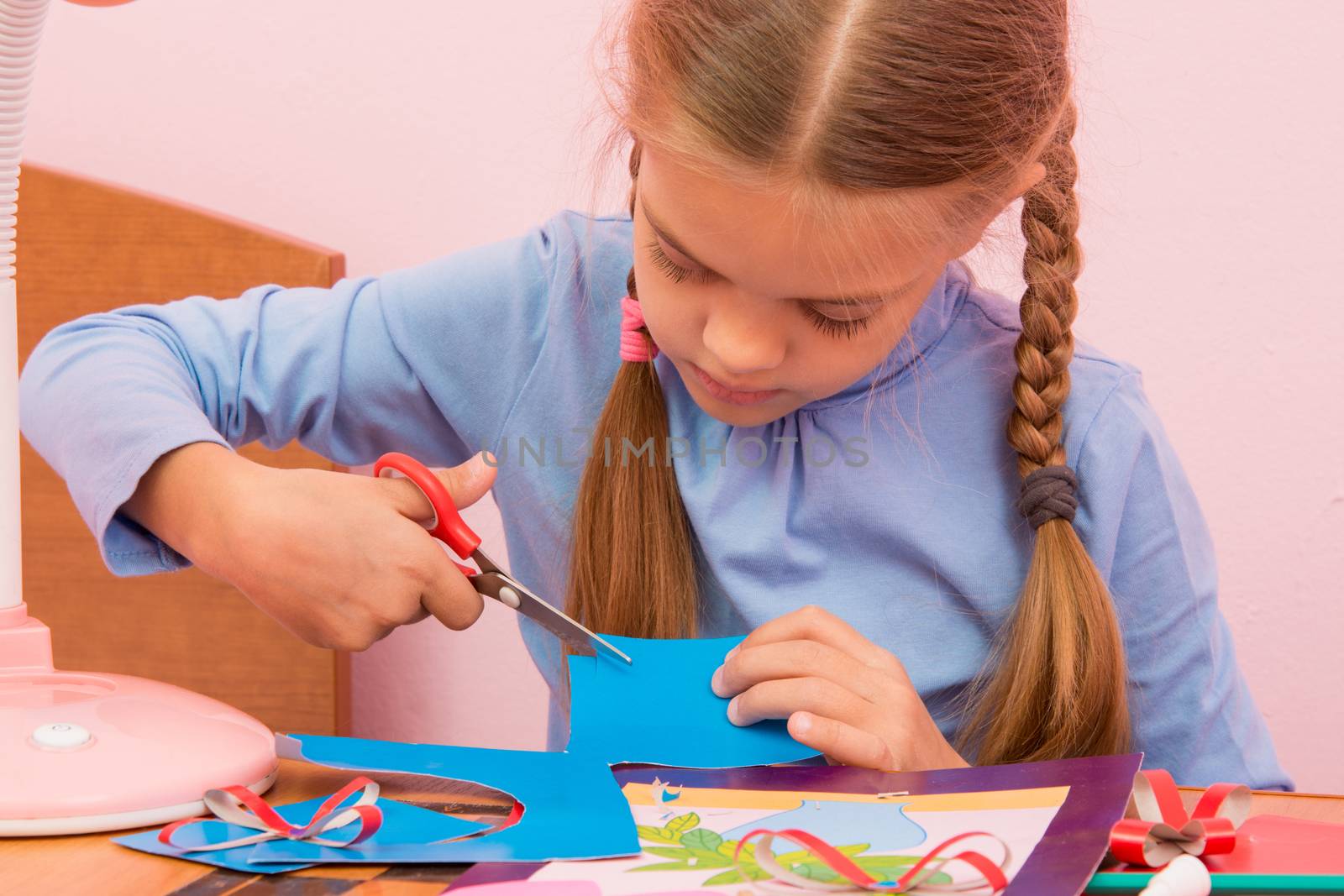 The child cuts off a piece of the blue colored cardboard