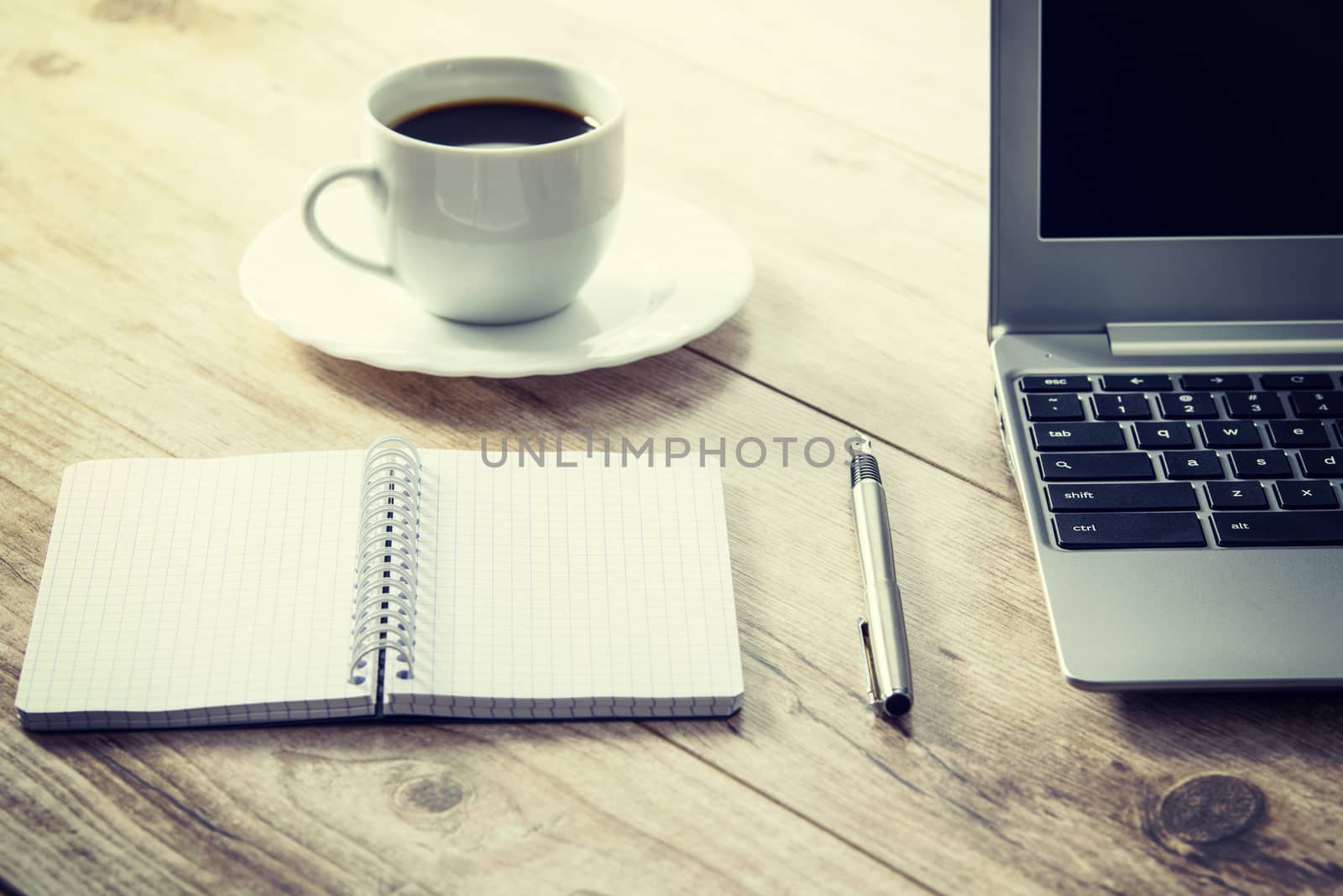 Blank notepad and a pen next to a laptop and coffee on a wooden vintage desk