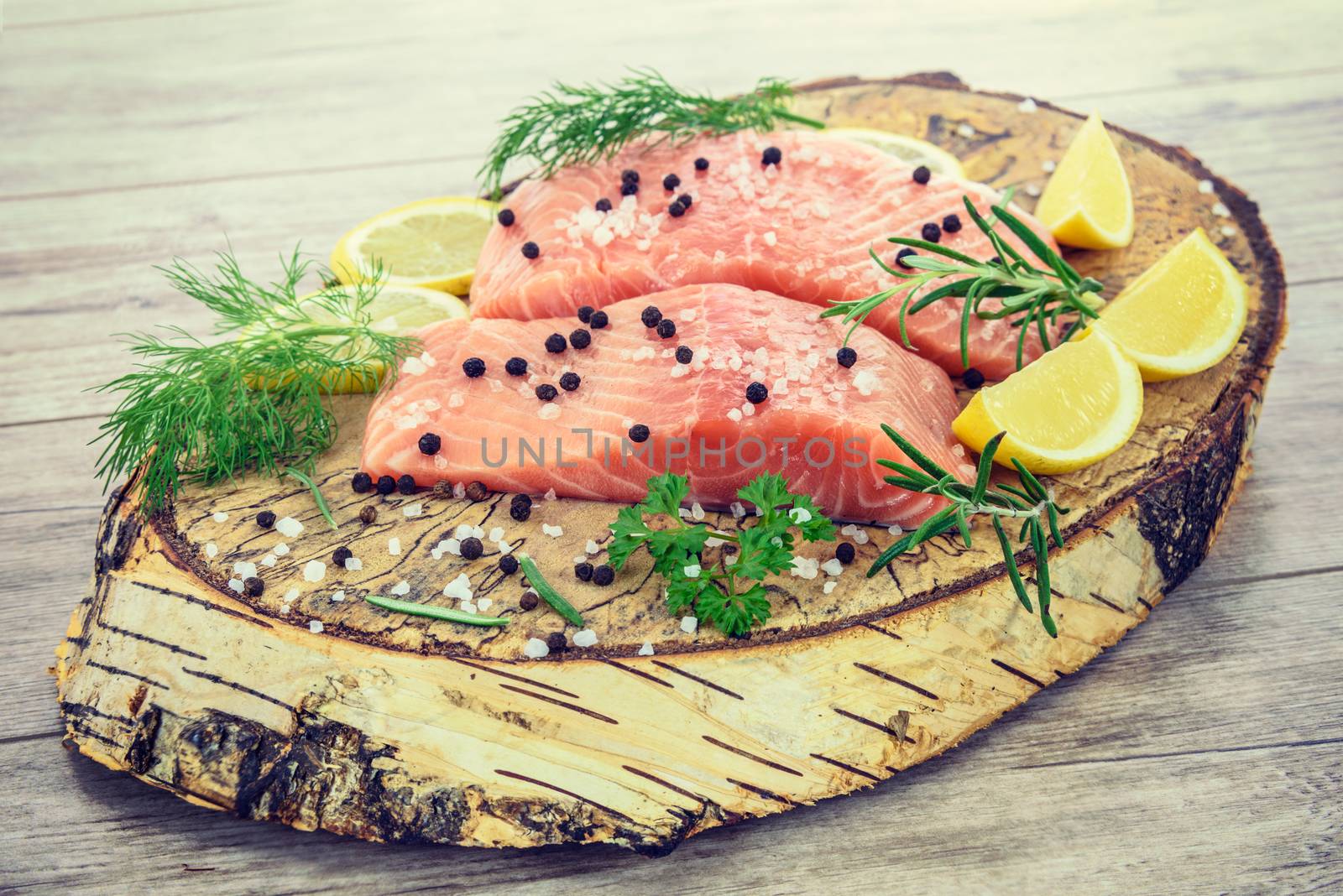 Shot of fresh Salmon steak on wooden birch stump pickled lemon, pepper, sea salt, rosemary, parsley, dill