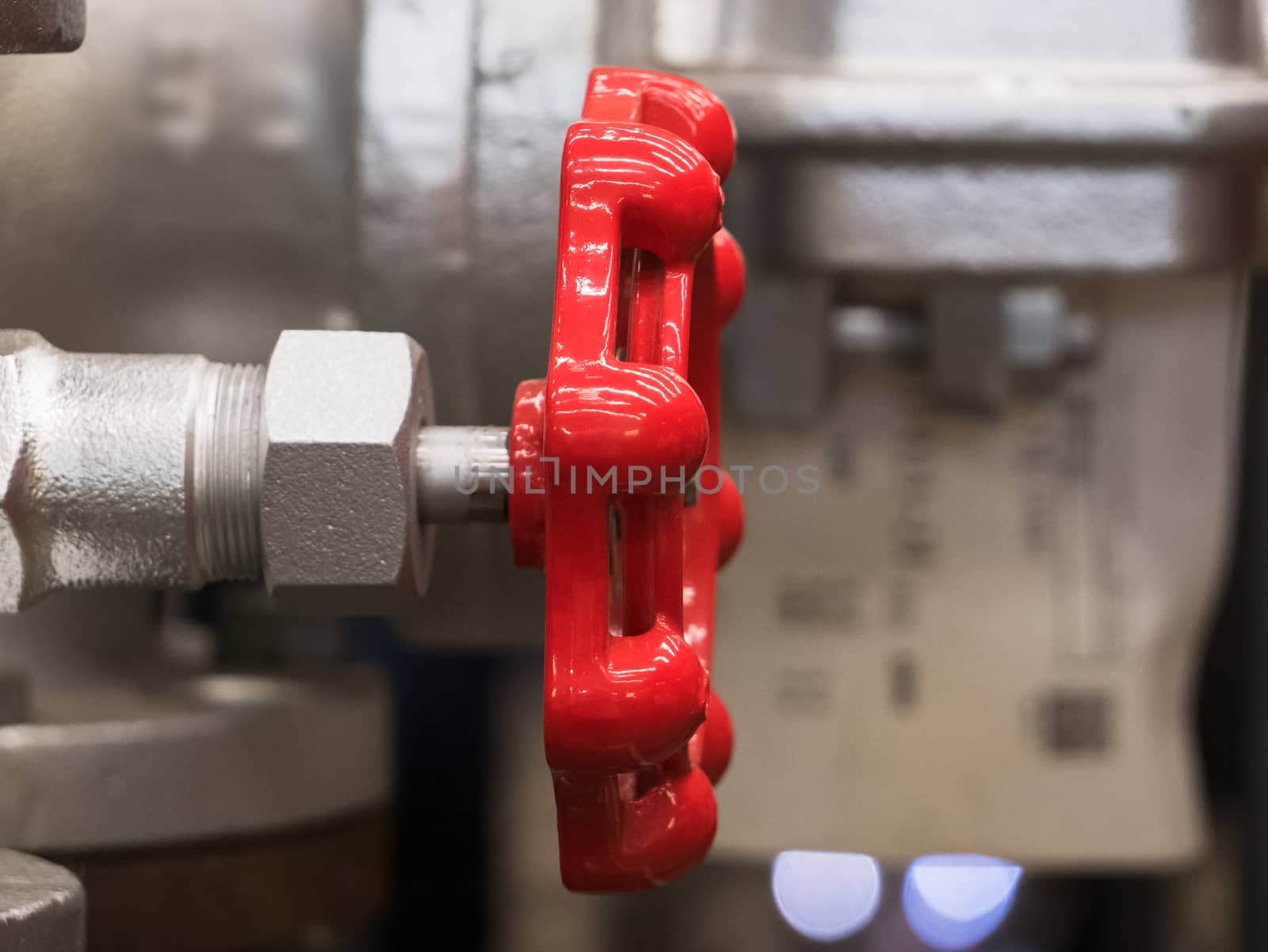 Red valve handle in industrial environment. Shallow depth of field with only the handle in focus.